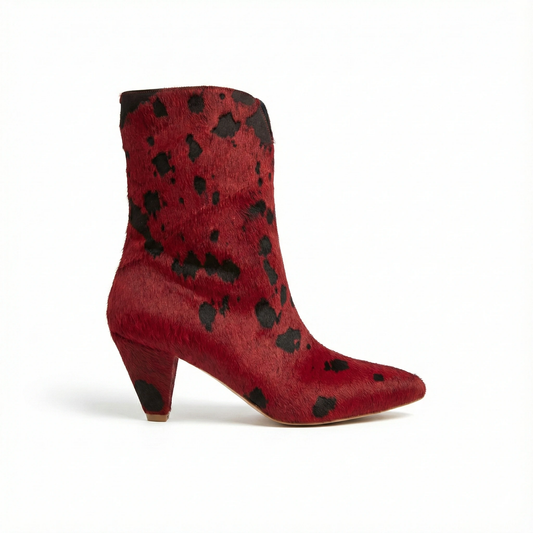 Red pony-hair ankle boot with irregular black spots, pointed toe and chunky mid-height heel, side view.
