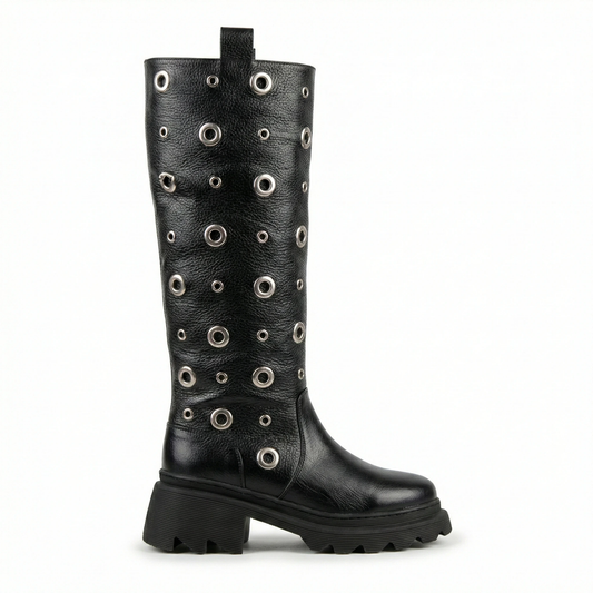 Black knee-high leather boot covered in silver grommets with a chunky platform sole and lug tread, pull tab at top.